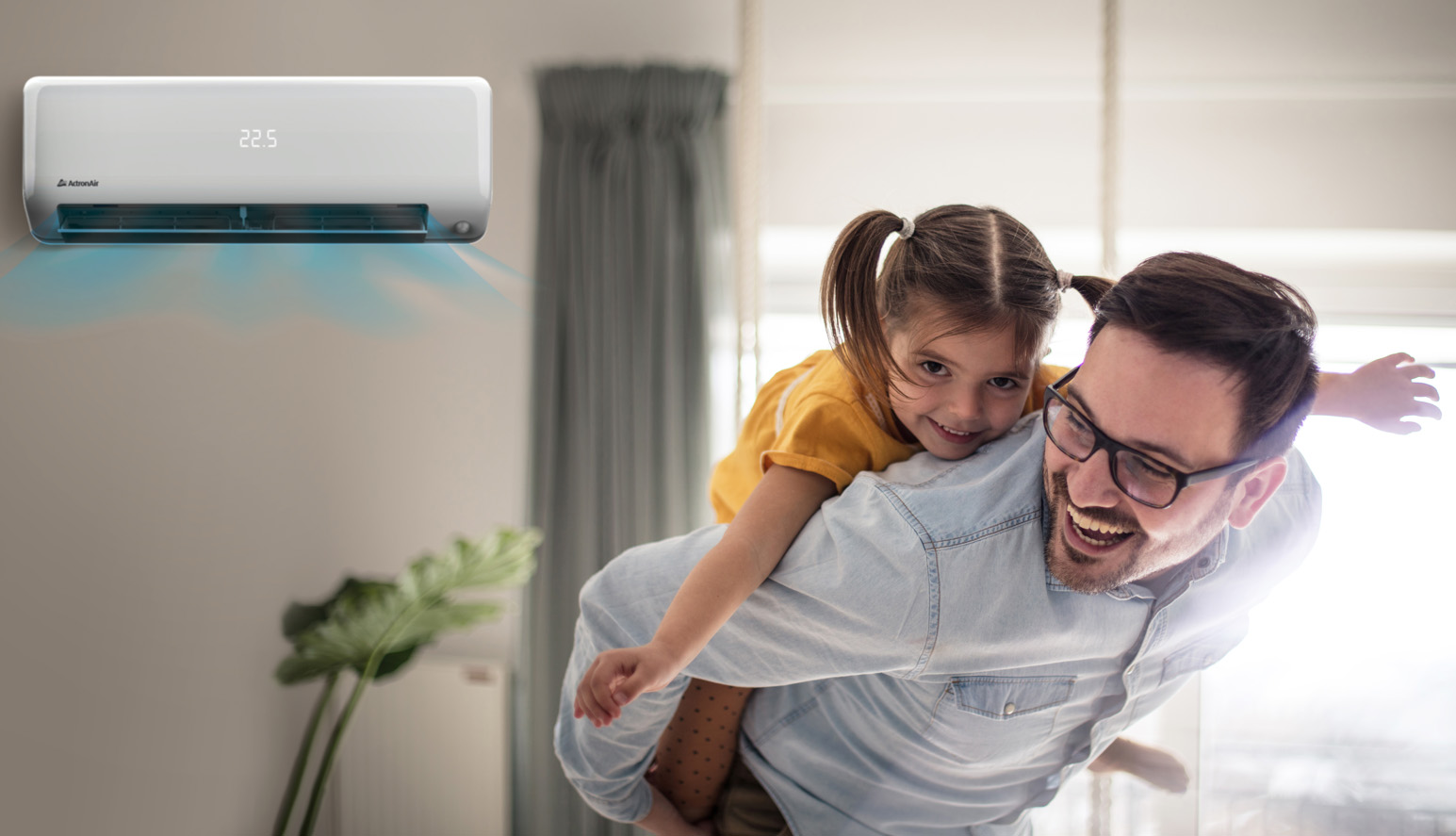 A smiling man gives a piggyback ride to a laughing young girl inside a bright room, with an air conditioner displaying 22.5°C—perfect for enjoying comfort whilst taking advantage of an appliance rebate.