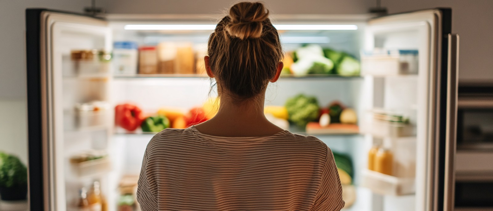A woman looking at a fridge, considering an appliance cashback to save on her purchase.